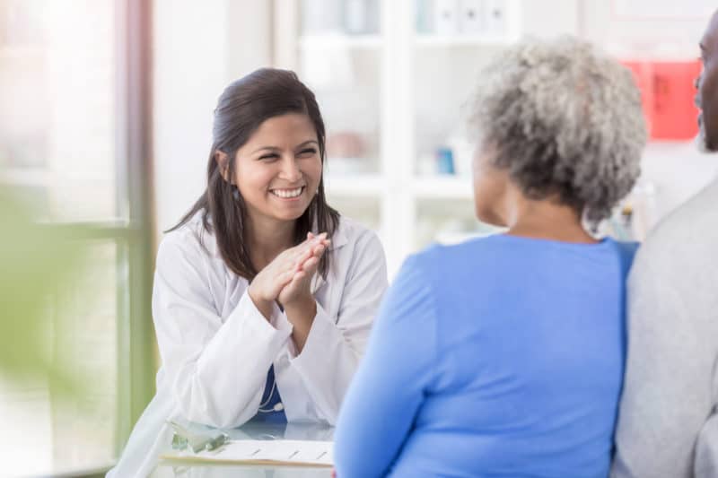 Doctor sits at her desk across from senior couple